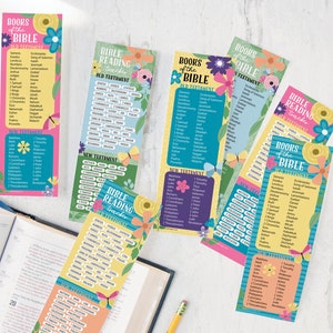 May include: A collection of colorful Bible reading tracker bookmarks. Each bookmark features a list of books from the Old and New Testaments, with floral and butterfly designs. The bookmarks are on a white surface next to an open book.