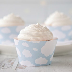 Op de afbeelding: Drie witte cupcakes met witte frosting in blauwe cupcakevormpjes met een wit wolkenpatroon.
