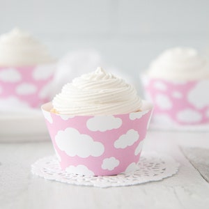 May include: Pink cupcake liners with a white cloud pattern. The liners are filled with white frosting and are displayed on a white surface.