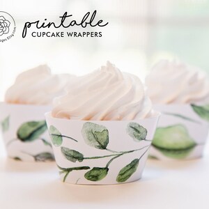 May include: Three cupcakes with white frosting in decorative paper wrappers. The wrappers have a watercolour design of green leaves and branches on a white background. The text "printable CUPCAKE WRAPPERS" is visible.