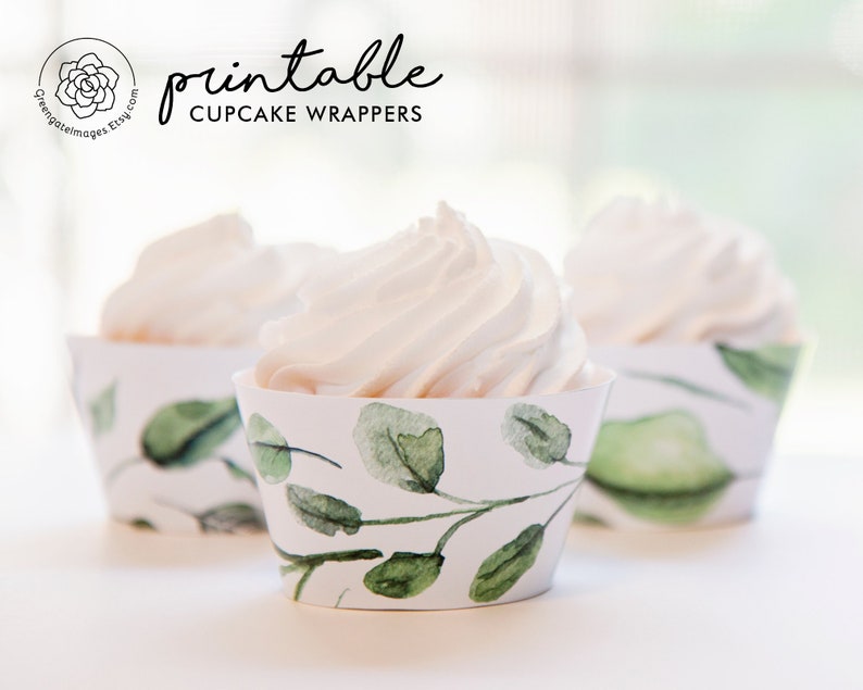 May include: Three cupcakes with white frosting in decorative paper wrappers. The wrappers have a watercolour design of green leaves and branches on a white background. The text "printable CUPCAKE WRAPPERS" is visible.