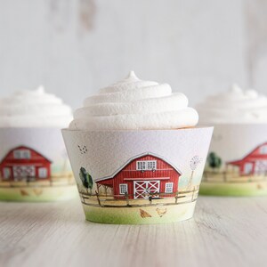 May include: Three white frosted cupcakes with red barn cupcake wrappers. The wrappers feature a red barn with white windows and a white fence. There are green trees and a windmill in the background.