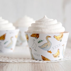 May include: White cupcake with white frosting decorated with a farm animal themed cupcake wrapper. The wrapper features a white background with illustrations of chickens, ducks, and geese.
