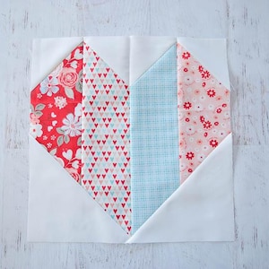 May include: A fabric heart quilt block with a white background. The heart is composed of red floral, red and white heart-patterned, light blue, and pink floral fabrics. The block is square and ready for quilting.