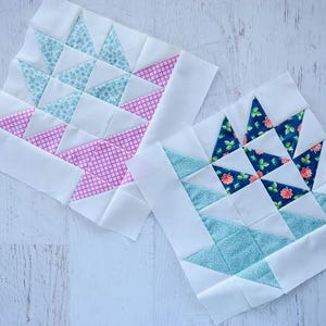 May include: Two handmade quilt blocks with a basket design. One block features light blue and pink patterned fabric triangles, while the other has blue floral and turquoise triangles. Both are set against a white background.