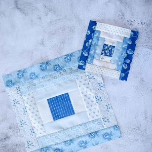 May include: Two handmade blue and white quilted squares. The larger square has a central blue square with white dotted lines, surrounded by white and patterned blue fabric. The smaller square has a similar design, with varying shades of blue.