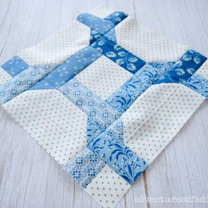 May include: A blue and white patchwork quilt block with a geometric design. The block is made of various fabrics with different patterns, including polka dots, floral prints, and solid colours.