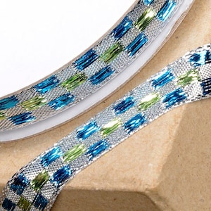 May include: Silver ribbon with a blue and green checkered pattern. The ribbon is metallic and has a shiny finish.