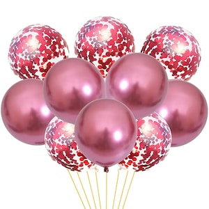 Può includere: Un set di nove palloncini, tra cui sei palloncini rosa metallizzati e tre palloncini trasparenti con coriandoli rossi. I palloncini sono legati insieme con uno spago dorato.
