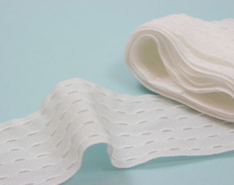 May include: A roll of white, textured ribbon with a repeating oval pattern. The ribbon is unrolled, revealing its woven texture and the details of the design. The background is a light blue.