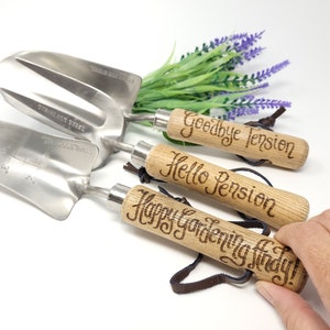 May include: Set of three gardening tools with wooden handles. The handles are engraved with the phrases "Goodbye Tension", "Hello Pension", and "Happy Gardening Lady!"