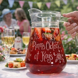 May include: A clear glass pitcher filled with a red beverage, sliced strawberries, and mint leaves. The exterior features white etched text that reads It's always Pimms Oclock at Kay's, surrounded by decorative floral and star-shaped line art designs.
