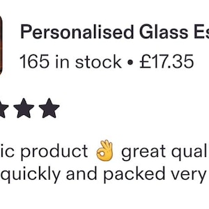 May include: A clear glass espresso cup and matching saucer set featuring the white text "Dad's Espresso" printed on the side of the cup. The cup is filled with dark brown coffee and is positioned next to several scattered roasted coffee beans.