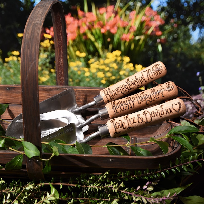 set of three garden tools with wooden handles and steel tops, a fork, a trowel a planter, hand engraved in a calligraphy font with the words Blooming lovely at 70, Mum x , We love you, or you can choose your own messages