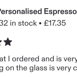 May include: A clear glass espresso cup featuring the text "Sam's espresso" etched on the front surface. The cup is positioned on a matching glass saucer, with a small wooden sign nearby that reads "for Mum" with a heart symbol, and coffee beans.