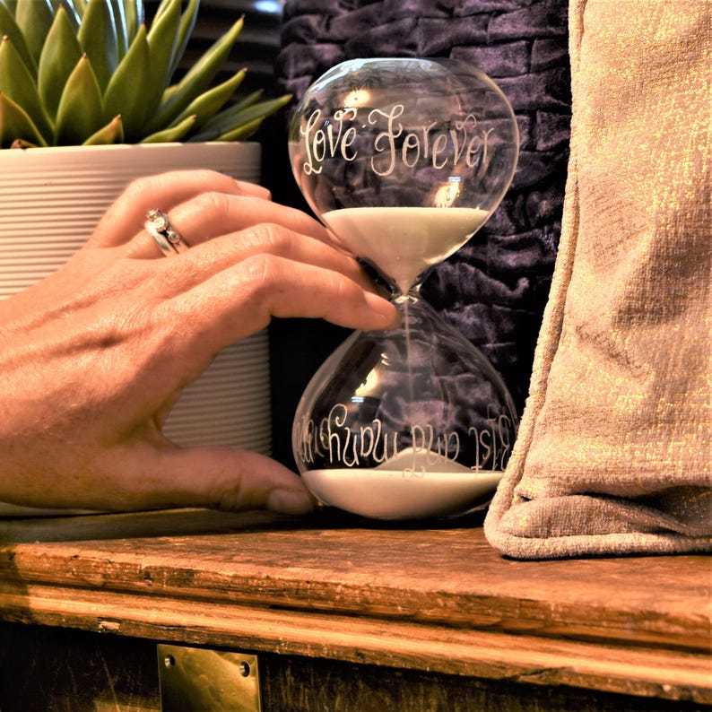 a sand timer ornament containing white sand has been engraved with a message saying 'love forever' in a calligraphy font