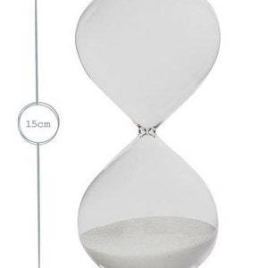 May include: Clear glass hourglass with white sand. The hourglass is 15cm tall and 7cm wide. The design features a classic shape with rounded top and bottom chambers connected by a narrow neck. The sand is visible inside the bottom chamber.