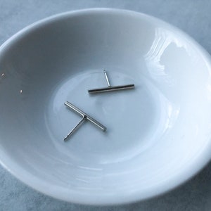 Peut inclure: Deux boucles d'oreilles en forme de barre argentées sur un plat en céramique blanche.
