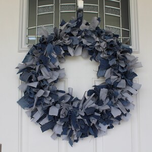 May include: A blue and gray denim wreath made from strips of fabric. The wreath is hanging on a white door.