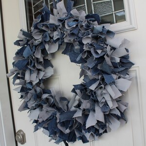 May include: A blue and gray denim wreath made from strips of fabric. The wreath is hanging on a white door.