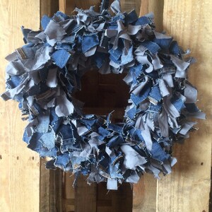 May include: A blue and gray denim wreath made from strips of fabric. The wreath is hanging on a wooden pallet.
