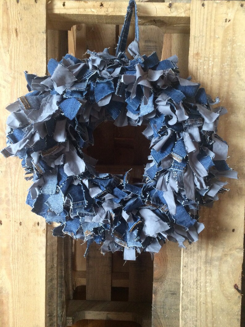 May include: A blue and gray denim wreath made from strips of fabric. The wreath is hanging on a wooden pallet.