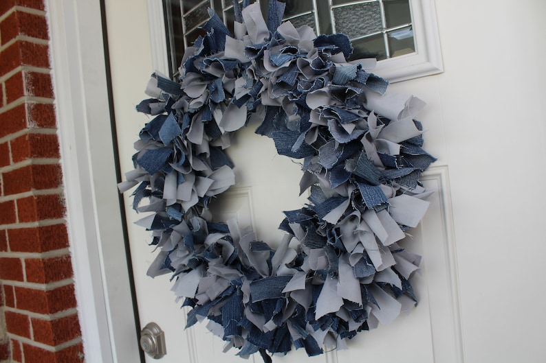 May include: A blue and gray denim wreath made from strips of fabric. The wreath is hanging on a white door.
