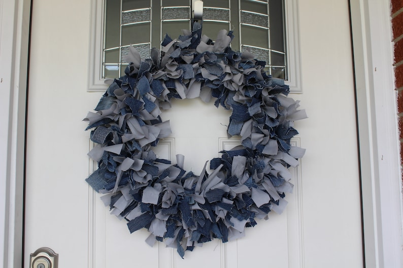 May include: A blue and gray denim wreath made from strips of fabric. The wreath is hanging on a white door.