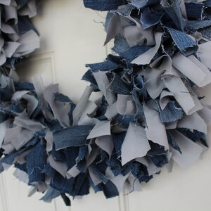 May include: A wreath made of blue and gray denim fabric scraps. The wreath is hanging on a white door.