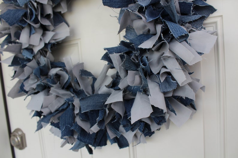 May include: A wreath made of blue and gray denim fabric scraps. The wreath is hanging on a white door.