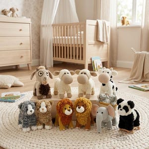 Op de afbeelding: Een verzameling handgemaakte knuffels, waaronder schapen, een koe, een panda, een leeuw en een olifant, gerangschikt op een crèmekleurig tapijt. De knuffels staan in een kinderkamer met een wieg en een commode.