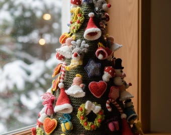 Op de afbeelding: Een handgemaakte, gehaakte kerstboom met diverse ornamenten. De boom is donkergroen en versierd met rode, witte en gele gehaakte decoraties, waaronder harten, sterren en kerstmutsen. Hij staat op een houten vensterbank.
