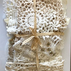 Puede incluir: Un paquete de encajes y tapetes y adornos de ganchillo blancos y crema. El paquete est&aacute; atado con una cinta de color beige claro, creando un paquete decorativo. Se pueden ver varias texturas y patrones, incluyendo dise&ntilde;os florales y geom&eacute;tricos.