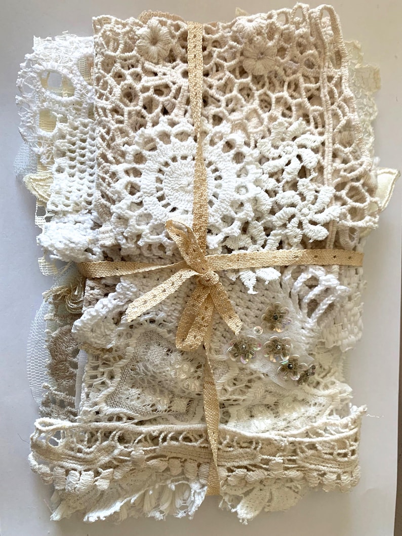 Puede incluir: Un paquete de encajes y tapetes y adornos de ganchillo blancos y crema. El paquete est&aacute; atado con una cinta de color beige claro, creando un paquete decorativo. Se pueden ver varias texturas y patrones, incluyendo dise&ntilde;os florales y geom&eacute;tricos.