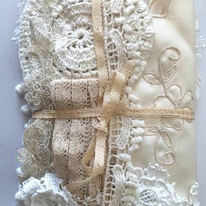 Puede incluir: Un conjunto de encajes y telas vintage en tonos crema y beige, atado con una cinta beige. El paquete incluye varios tapetes de ganchillo, tela bordada y adornos de encaje, creando una apariencia texturizada y en capas. La est&eacute;tica general es delicada y artesanal.