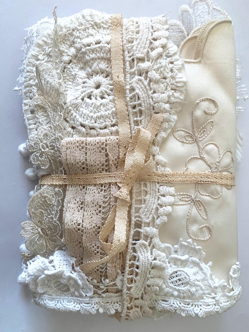 Puede incluir: Un conjunto de encajes y telas vintage en tonos crema y beige, atado con una cinta beige. El paquete incluye varios tapetes de ganchillo, tela bordada y adornos de encaje, creando una apariencia texturizada y en capas. La est&eacute;tica general es delicada y artesanal.