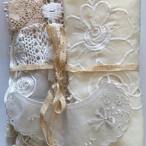 Puede incluir: Un conjunto de encajes y telas bordadas vintage en tonos crema y beige. El conjunto est&aacute; atado con una cinta de color beige claro. Se distinguen varias texturas: ganchillo, ojales y bordados florales, creando una est&eacute;tica antigua y delicada.