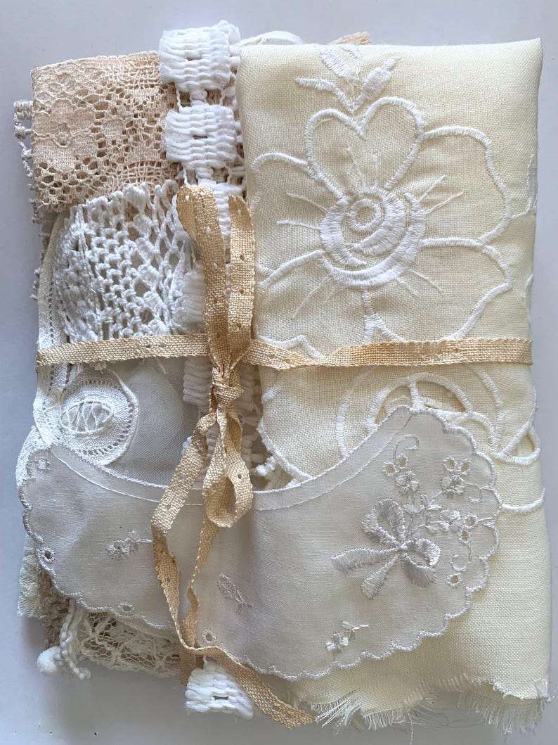 Puede incluir: Un conjunto de encajes y telas bordadas vintage en tonos crema y beige. El conjunto est&aacute; atado con una cinta de color beige claro. Se distinguen varias texturas: ganchillo, ojales y bordados florales, creando una est&eacute;tica antigua y delicada.