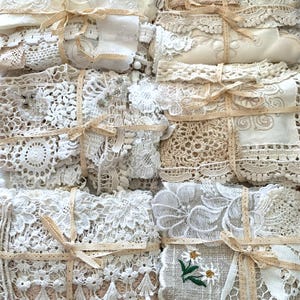 Puede incluir: Un surtido de paquetes de encaje y tela vintage atados con cintas beige. Los paquetes presentan varias texturas, incluyendo ganchillo, dise&ntilde;os florales bordados y delicados adornos de encaje. La paleta de colores es principalmente crema y beige.