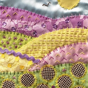May include: A textile artwork depicting a landscape with a blue sky, yellow sun, and rolling hills in pink, yellow, and green. Sunflowers are in the foreground. The text "Fairy Floss Laces" is at the top of the piece.