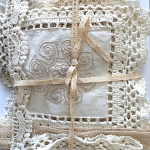 Puede incluir: Un conjunto de tapetes de encaje y ganchillo vintage en tonos crema y beige, atados con una cinta beige. Los tapetes presentan patrones y texturas intrincados, con un cuadrado central bordado con un dise&ntilde;o floral.