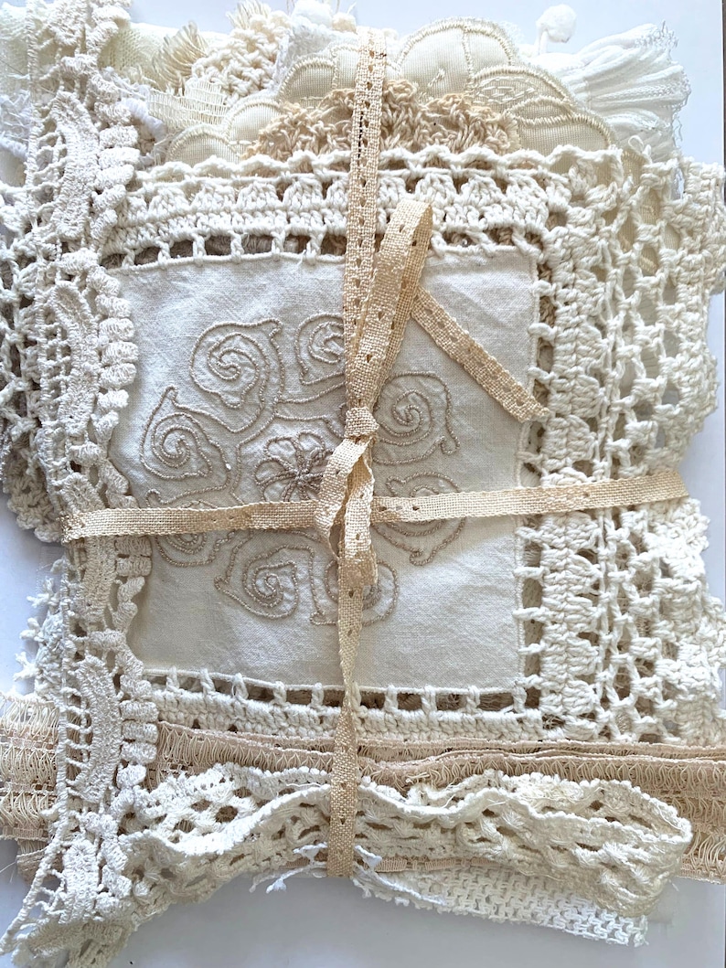 Puede incluir: Un conjunto de tapetes de encaje y ganchillo vintage en tonos crema y beige, atados con una cinta beige. Los tapetes presentan patrones y texturas intrincados, con un cuadrado central bordado con un dise&ntilde;o floral.