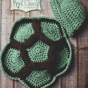 May include: A handmade crochet turtle costume set in shades of green and brown. The set includes a turtle shell and a matching hat. The shell is designed with a segmented pattern, and the hat has a rounded shape. The text "Knot Crazy" is visible.
