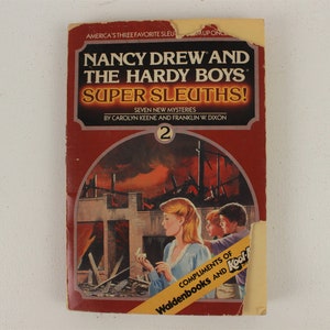 May include: A red paperback book with the title "Nancy Drew and the Hardy Boys Super Sleuths!"  The book cover features an illustration of three children standing in front of a burning building. The book is number 2 in a series of seven new mysteries by Carolyn Keene and Franklin W. Dixon.