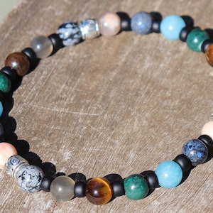 May include: A beaded bracelet with a variety of stones, including blue, green, brown, and grey. The bracelet has silver accents and black spacers.