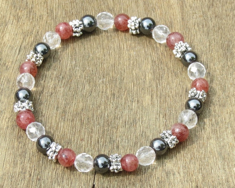 K&ouml;nnte beinhalten: Ein Armband mit roten, klaren und schwarzen Perlen. Die roten Perlen haben ein gesprenkeltes Aussehen, w&auml;hrend die klaren Perlen facettiert sind. Die schwarzen Perlen sind durch silberfarbene Abstandshalter getrennt, was einen Kontrast in Textur und Farbe erzeugt.