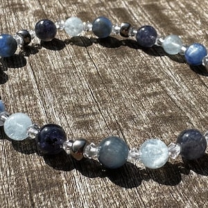 Può includere: Un braccialetto di pietre blu e bianche con perline d'argento. Il braccialetto è realizzato con perline di acquamarina, cianite e quarzo trasparente.