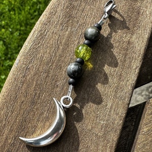 May include: A silver crescent moon charm with a black and green beaded chain. The chain has a silver clasp.