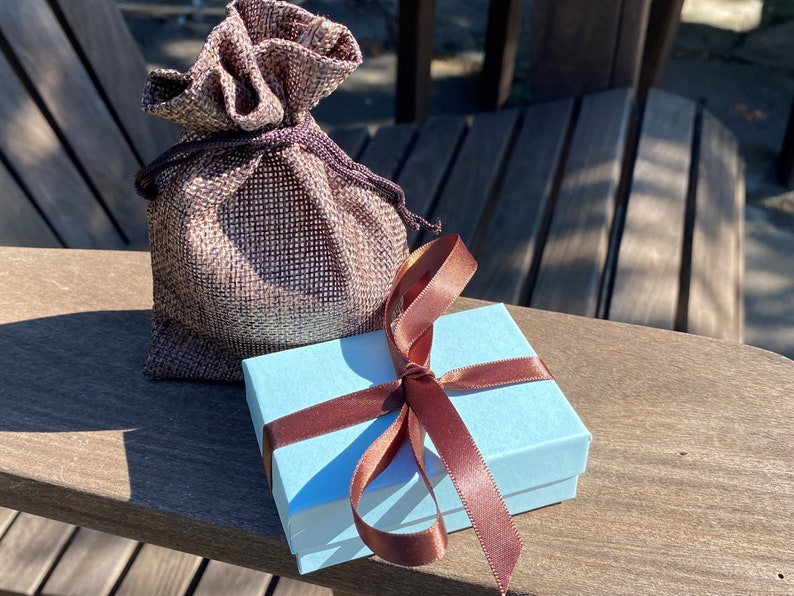 May include: A light blue gift box with a brown satin ribbon tied in a bow. The box is sitting on a wooden surface next to a brown burlap bag.