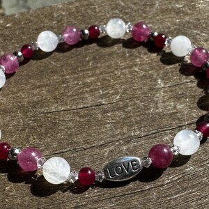 May include: A white and pink beaded bracelet with a silver charm that says "LOVE".